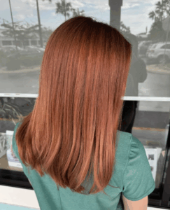 Person with straight, shoulder-length reddish-brown hair wearing a green shirt, standing outdoors facing away from the camera. - Escape Salon | Nokomis, FL